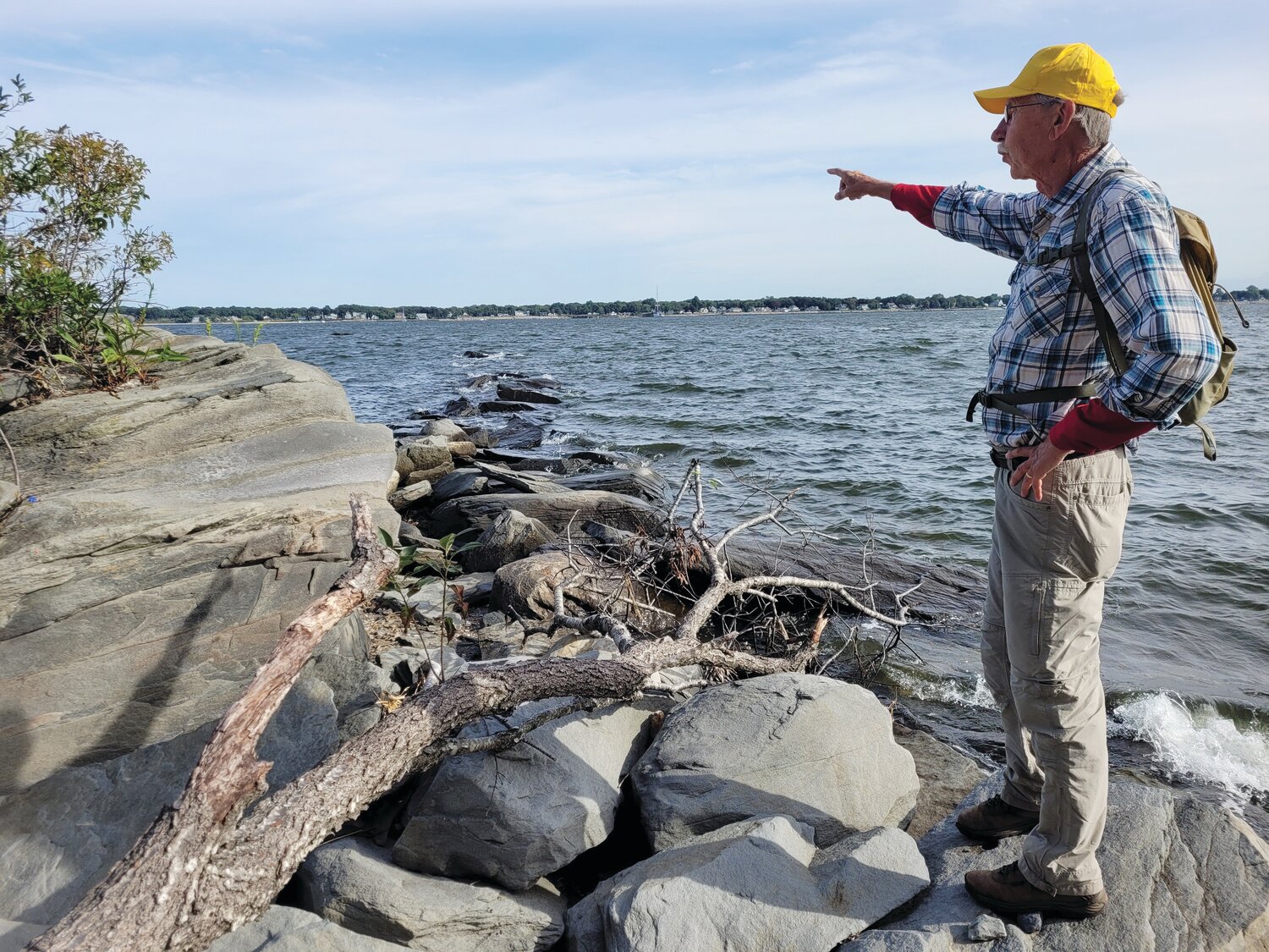 RI’S FIRST LOST AVIATOR: John Kostrzewa points across the row of Sally Rocks, which stretch from the Goddard Memorial State Park beach in Warwick and into Greenwich Bay. The author discovered a WWI seaplane manufacturer set up operations a century ago on Chepiwanoxet Point, and he eventually learned and wrote about a  test pilot who lost his life on these same choppy waters.